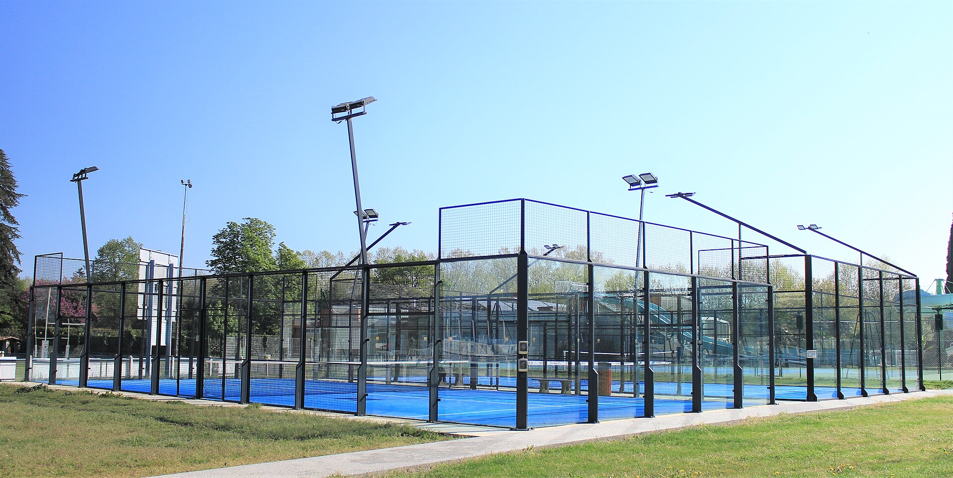 An outdoor padel court with glass walls and floodlights, illustrating the sport for players near Bath