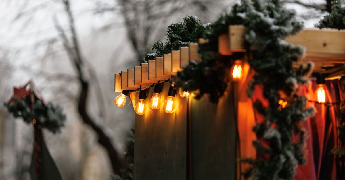 Warm string lights and pine garland on a snow-dusted wooden market stall at dusk.