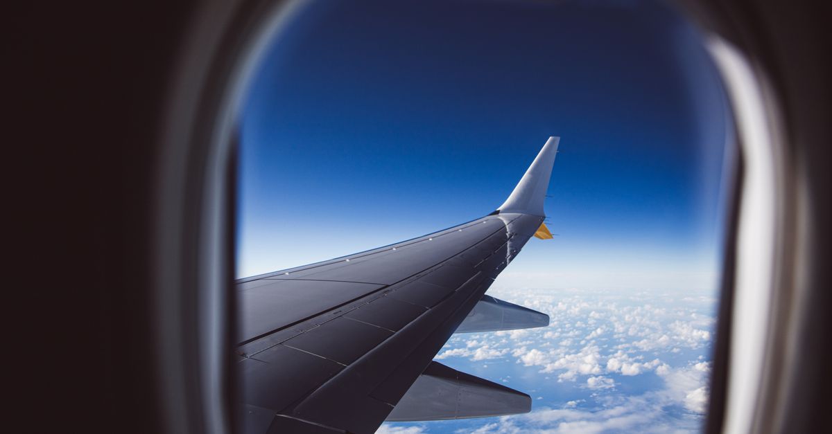 View of an aircraft wing above clouds, seen through the cabin window.