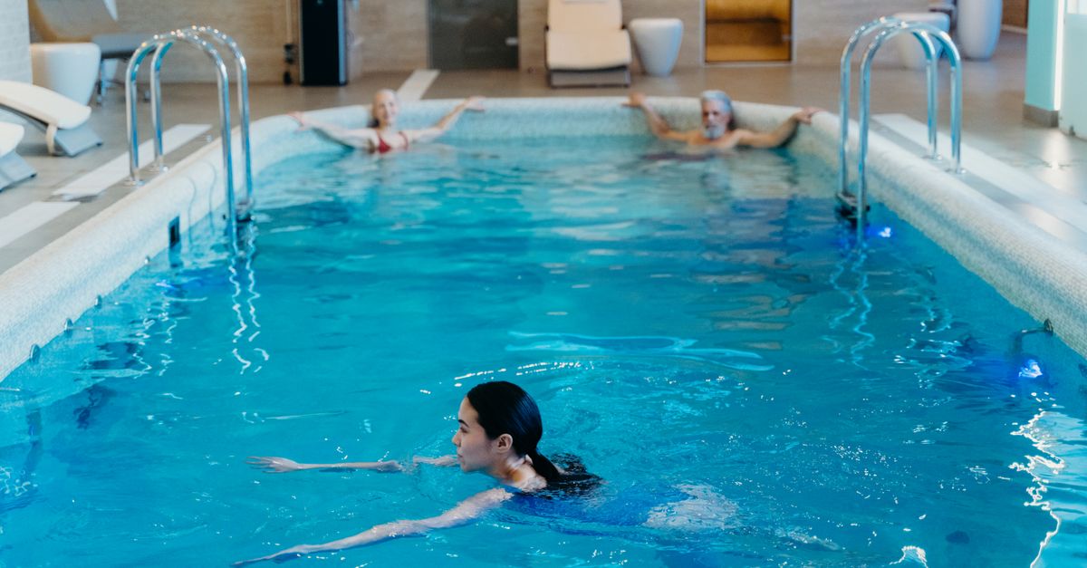 People bathing and relaxing in a calm, steam-lit indoor swimming pool.