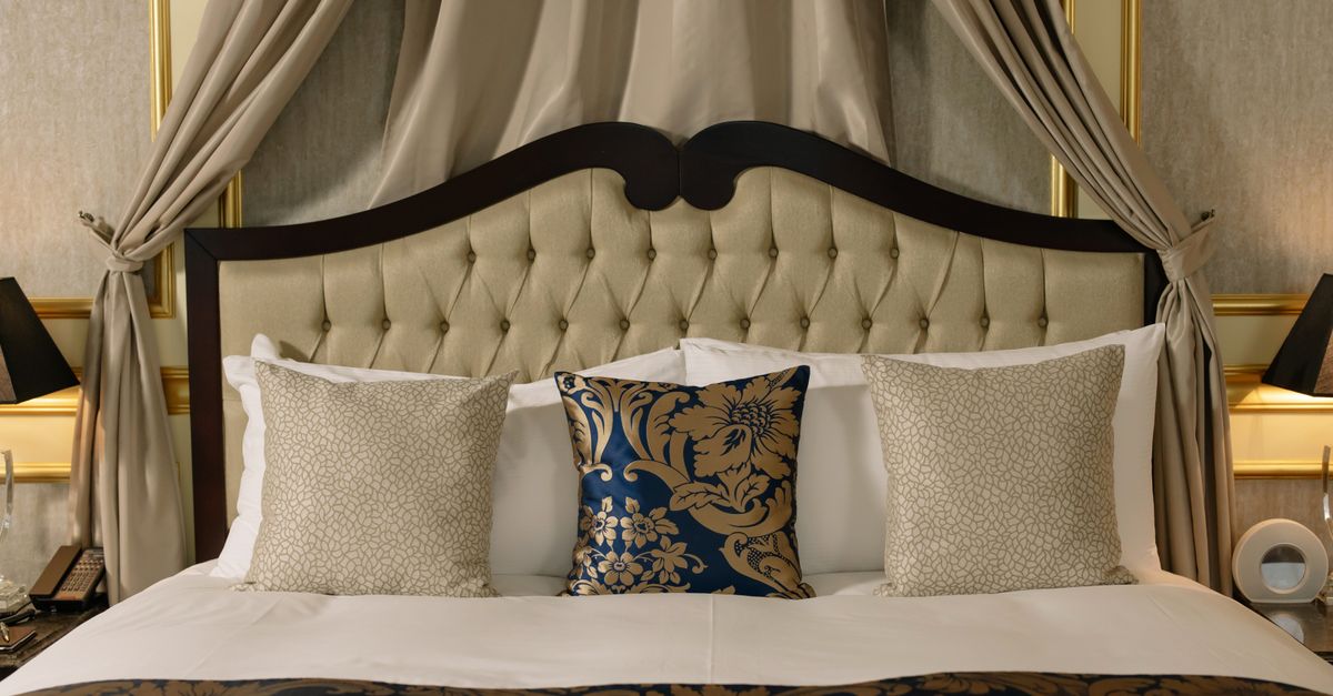 An elegant tufted headboard hotel bed dressed with gold and navy cushions.
